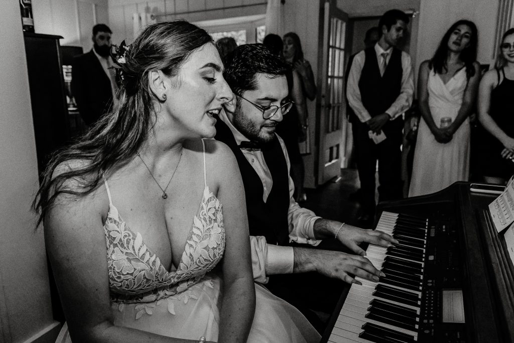 bride and groom singing and playing the piano at their home wedding for their wedding guests photographed by intimate wedding photographer heather doughty photography