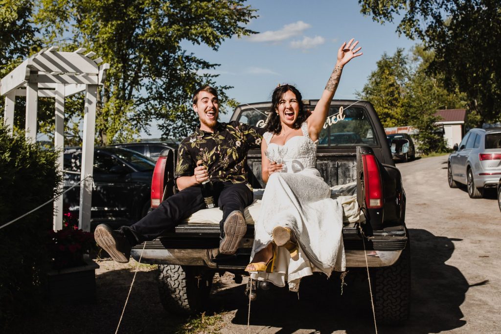 wedding couple leaving their wedding in the back of a pick up truck, yelling and cheering at their house wedding in cobourg, ontario